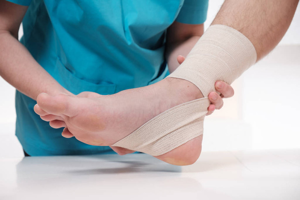 Female doctor bandaging foot of male patient - Foto, Imagen