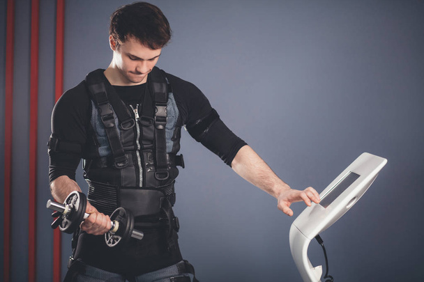 человек в костюме электрической мышечной стимуляции, стоящий с гантелями
 - Фото, изображение