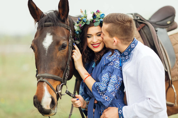 Ο φίλος φιλιά την κοπέλα που χαμογελάει πραγματικά και κατέχει το άλογο για ένα χαλινάρι - Φωτογραφία, εικόνα