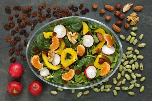 Gezond vegan salade met radijs, noten, gele sambal op donkere leisteen met kopie ruimte - Foto, afbeelding
