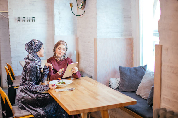 Two Muslim women in cafe, shop online using electronic tablet - Фото, изображение
