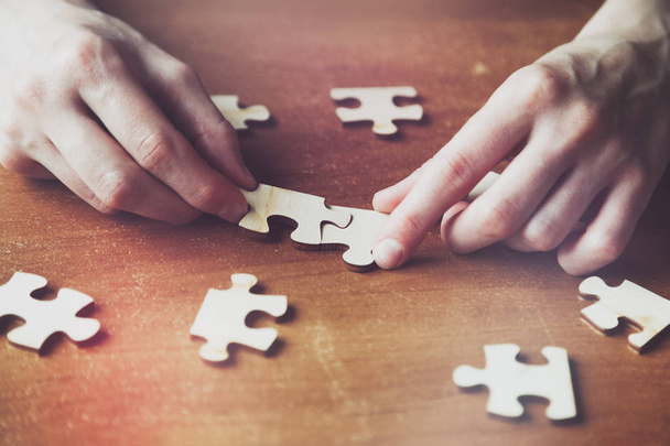 hands solving jigsaw puzzle with wooden pieces - 写真・画像