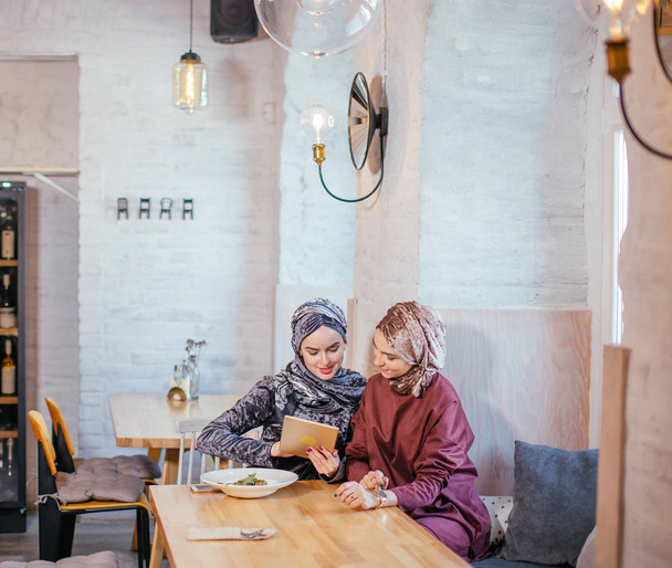 Two Muslim women in cafe, shop online using electronic tablet - Photo, image