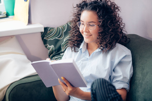 woman with curly hair in casual clothers reading book at home - Fotografie, Obrázek