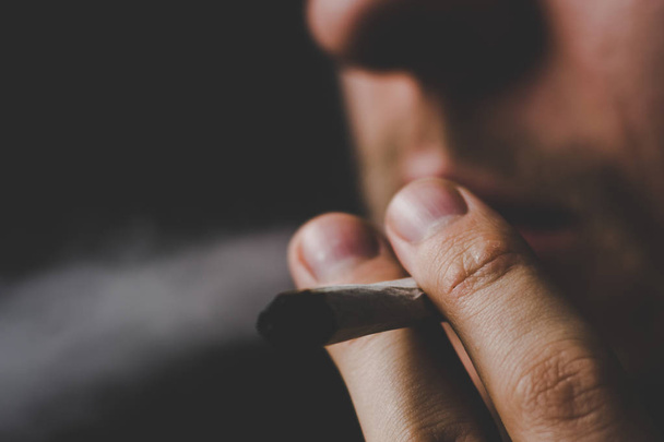 Un uomo fuma erba di cannabis, una canna e un accendino in mano. Fumo su fondo nero. Concetti di uso medico di marijuana e legalizzazione della cannabis
. - Foto, immagini