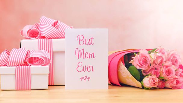 Äitienpäivä lahja, vaaleanpunaisia ruusuja ja paras äiti koskaan onnittelukortti pöydällä
. - Valokuva, kuva