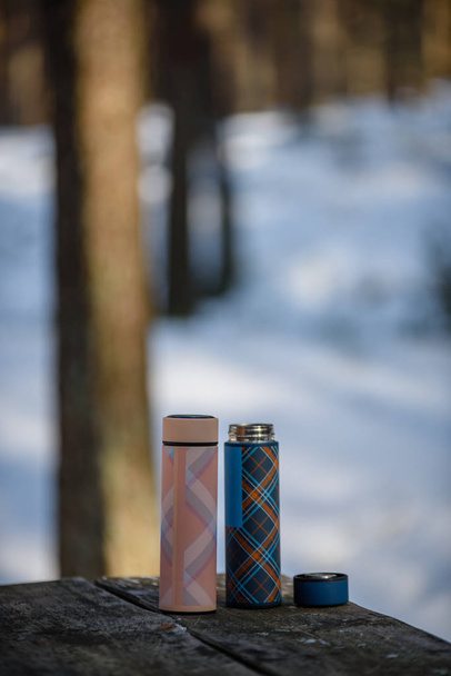 πολύχρωμο thermoses στο ξύλινο τραπέζι στο δάσος του χειμώνα - Φωτογραφία, εικόνα