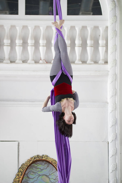 Atractiva gimnasta de aire cuelga boca abajo la realización de un hermoso elementos en la seda aérea
 - Foto, Imagen