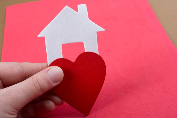 Pequena casa cortada de papel e um coração na mão em vista
 - Foto, Imagem