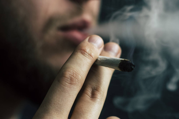 医療マリファナの使用と大麻の合法化の概念。黒の背景にたばこを吸います。男は、彼の手で大麻雑草、ジョイント、ライターにたばこを吸う. - 写真・画像