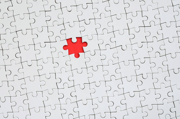 The texture of a white jigsaw puzzle in an assembled state with one missing element forming a red space - Foto, Bild