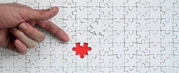 La trama di un puzzle bianco nello stato assemblato con un elemento mancante, formando uno spazio rosso, indicato dal dito della mano maschile
 - Foto, immagini