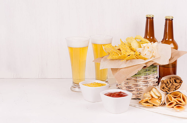 Summer fast food - different crunchy snacks, two lager beer in glass and brown bottles on soft white wood board.  - 写真・画像