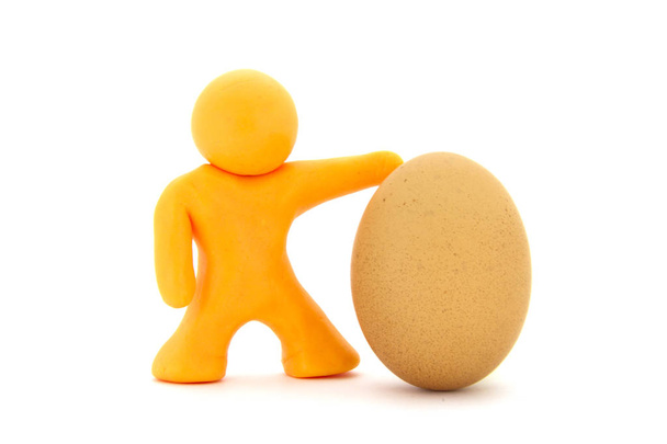 Orange plasticine character and single fresh chicken egg. Isolated over white background - 写真・画像