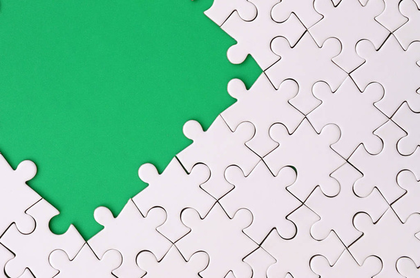Фрагмент сложенной белой головоломки на фоне зеленой пластиковой поверхности. Текстурная фотография с местом для копирования текста
 - Фото, изображение