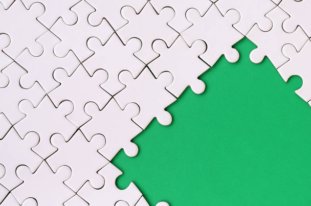 Фрагмент сложенной белой головоломки на фоне зеленой пластиковой поверхности. Текстурная фотография с местом для копирования текста
 - Фото, изображение
