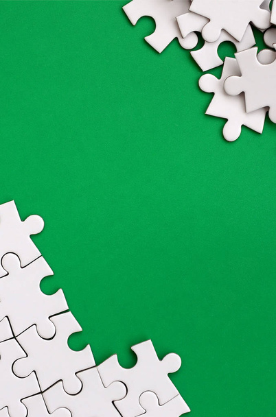 Fragment of a folded white jigsaw puzzle and a pile of uncombed puzzle elements against the background of a green surface. Texture photo with space for text - Photo, Image