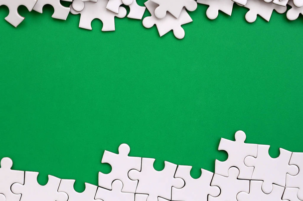 Fragment van een gevouwen witte puzzel en een stapel van niet-gekamde puzzel elementen tegen de achtergrond van een groene oppervlak. Textuur foto met ruimte voor tekst - Foto, afbeelding