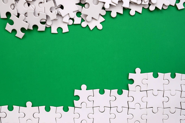 Fragment d'un puzzle blanc plié et une pile d'éléments de puzzle non peignés sur le fond d'une surface verte. Texture photo avec espace pour le texte
 - Photo, image