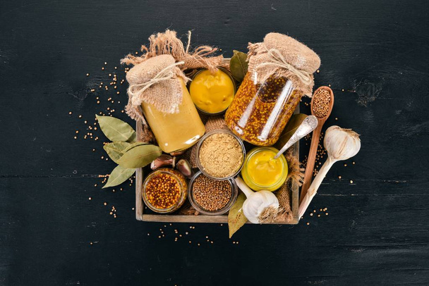A set of mustard in a wooden box. Spices On a black wooden background. Top view. Copy space for your text. - Foto, imagen