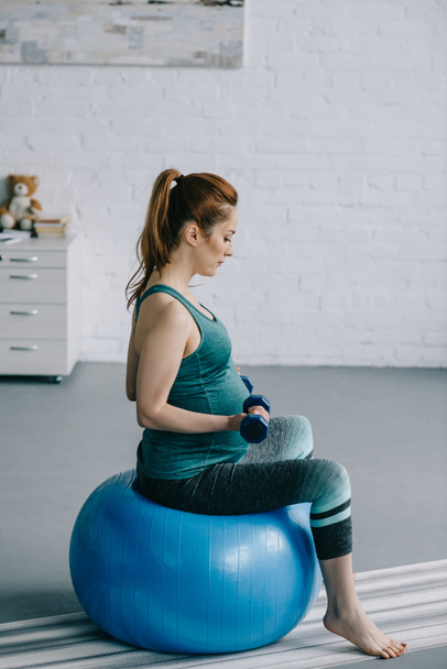 vue latérale de belle femme enceinte faisant de l'exercice avec haltères sur balle de fitness dans le salon
 - Photo, image