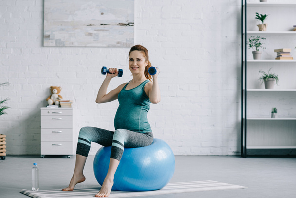 güzel bir hamile kadın fitness Ball oturma odasında dumbbells ile egzersiz - Fotoğraf, Görsel