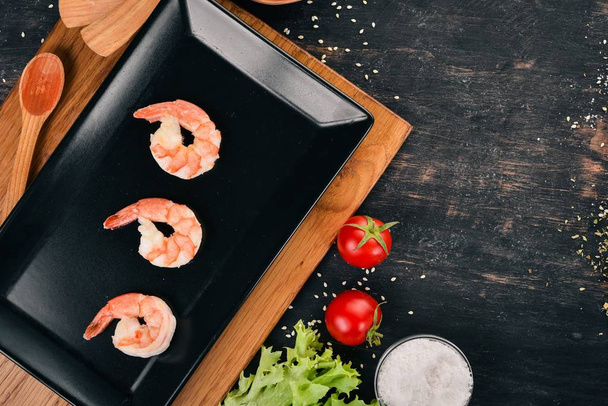 Large shrimps and plates. On a wooden background. Top view. Copy space for your text. - Фото, изображение