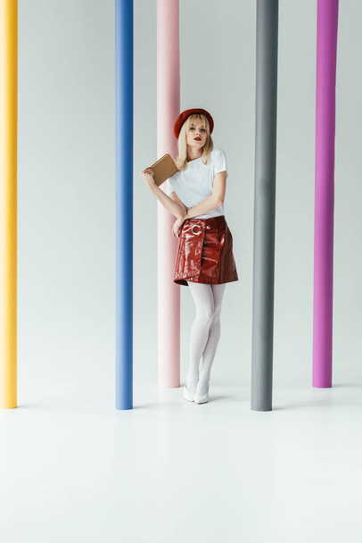 Attractive young woman holding book and posing by colorful pillars - Fotografie, Obrázek