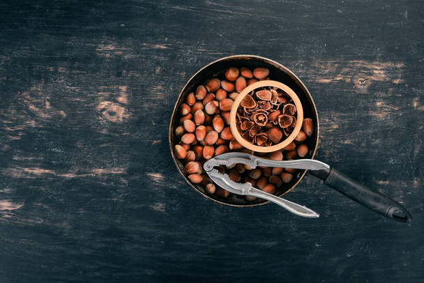 Hazelnut in a frying pan. On a black wooden background. Top view. Copy space for your text. - Zdjęcie, obraz
