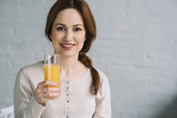beautiful woman holding glass of orange juice and looking at camera - Photo, Image