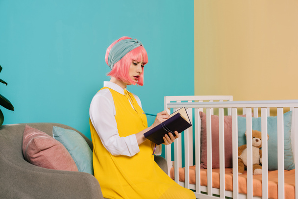 mujer embarazada estilo retro pin up con pelo rosa escribir algo para portátil en la habitación de los niños
 - Foto, imagen