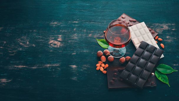 A glass of cognac, brandy, whiskey and a set of chocolate with cookies and sweets. On a black wooden background. Copy space for text. - Фото, зображення