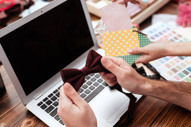 Man holding bow tie near woman hands with colorful samples on laptop background - Valokuva, kuva