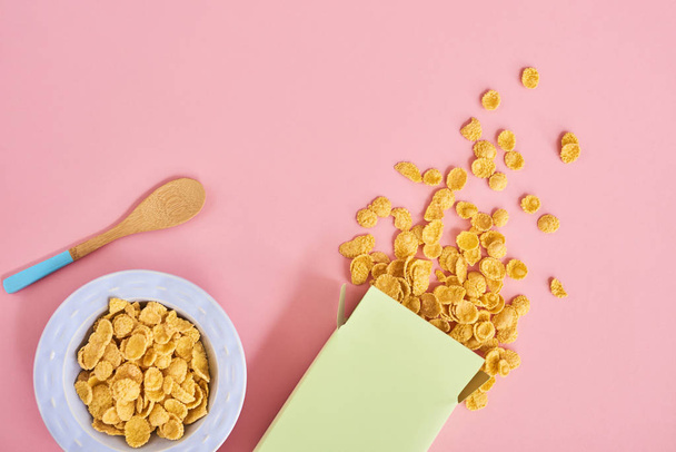 Vista dall'alto di scatola verde di cereali, piatto blu e cucchiaio di legno su sfondo rosa
 - Foto, immagini