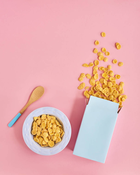 Vista superior de la caja azul de cereales, plato azul y cuchara de madera sobre fondo rosa
 - Foto, Imagen