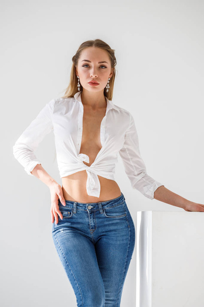 Portrait of sexy blonde girl wearing blue jeans and white shirt standing on white studio background - Foto, Bild