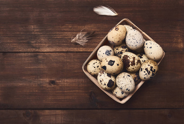 Top view of quail fresh eggs in wooden box and feathers on rustic wooden background. - Фото, изображение