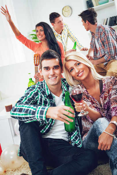 Young couple at home party toasting with drinks, smiling and looking at camera - Photo, Image
