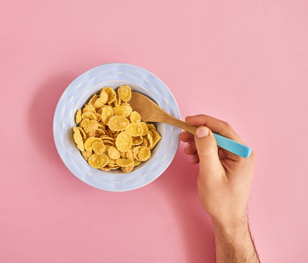 Placa azul de cereales y cuchara de mano masculina sobre fondo rosa
 - Foto, imagen