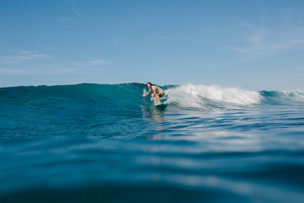 hombre joven en camiseta mojada montando olas azules en la tabla de surf durante sus vacaciones
 - Foto, Imagen