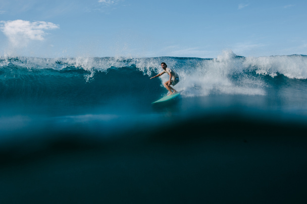 hombre en camiseta mojada montando grandes olas del océano en la tabla de surf en el día soleado
 - Foto, imagen