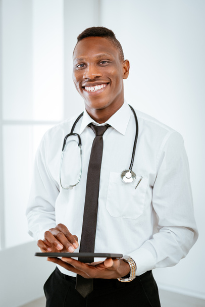Portret van jonge Afrikaanse lachende arts met de stethoscoop - Foto, afbeelding