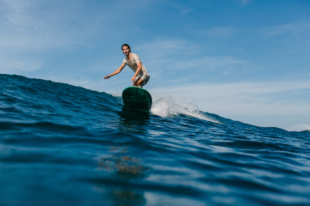 jongeman paardrijden golven op een surfplank op zonnige dag - Foto, afbeelding