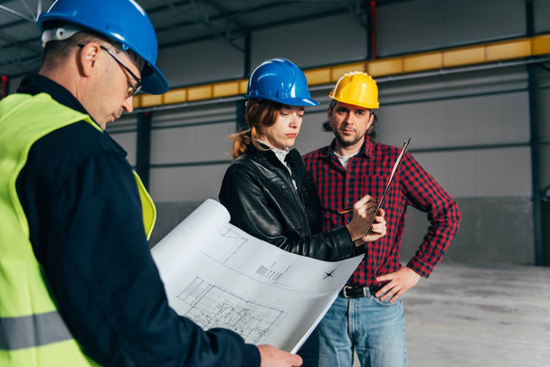Inspecteur de chantier faisant rapport d'inspection dans un grand hall industriel et discutant avec les travailleurs de la construction
 - Photo, image