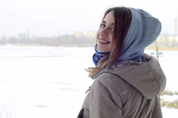 Uma jovem e sorridente menina caucasiana olha ao redor da linha do horizonte entre o céu eo lago congelado no tempo de inverno
 - Foto, Imagem