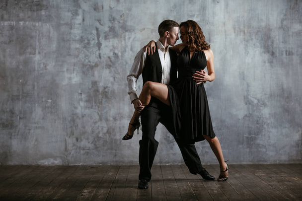 Jonge mooie vrouw in zwarte jurk en man dance tango - Foto, afbeelding
