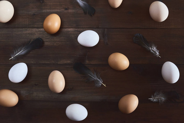Seamless pattern with fresh chicken eggs and feathers on dark wooden background. - 写真・画像