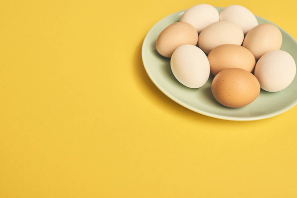 Huevos frescos de pollo crudo en plato verde sobre fondo amarillo
. - Foto, Imagen