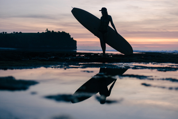 sylwetka młoda kobieta z deską surfingową na seashore wieczorem - Zdjęcie, obraz