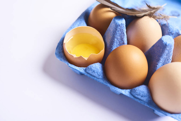 Vista da vicino delle uova di pollo marroni fresche in scatola di cartone blu con piume isolate su sfondo bianco
. - Foto, immagini